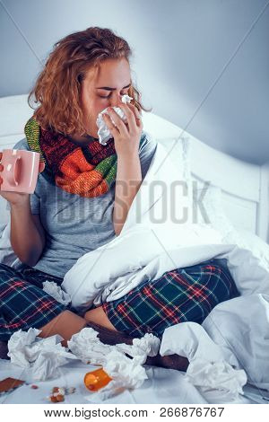 Attractive Blond Girl Blows Her Nose In The Napkin While Sitting On The Bas And Holding A Cup With W