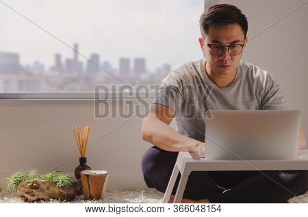 Asian Man In Casual Wear Sitting And Working On Laptop In Room That Have Candle, Aroma Diffuser And 
