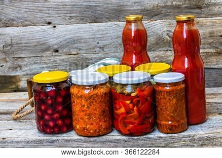 Jars With Variety Of Canned Vegetables And Fruits, Jars With Zacusca And Bottles With Tomatoes Sauce