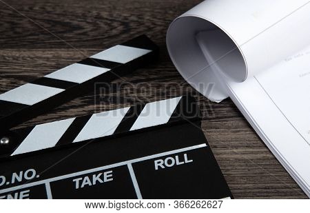 Black Movie Clapper With A Script Sheets On A Wooden Table Closeup