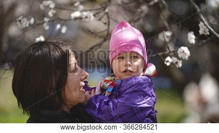 Beautiful Young Mom With Cute Daughter In Red Hat In A Park Near A Flowering Tree In Spring. Concept