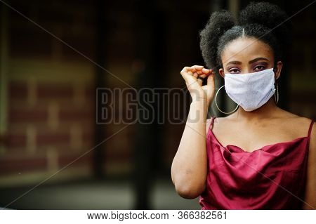 Covid-19, Infectious Virus. African Woman With Curly Hair, Wears Red Silk Dress And Medical Disposab