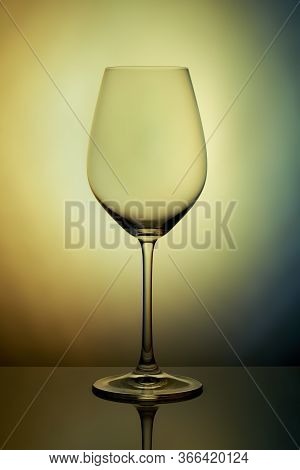 The Crystal Glass Stands On The Reflecting Surface On A Yellow Graybackground. Studio Photo. Product