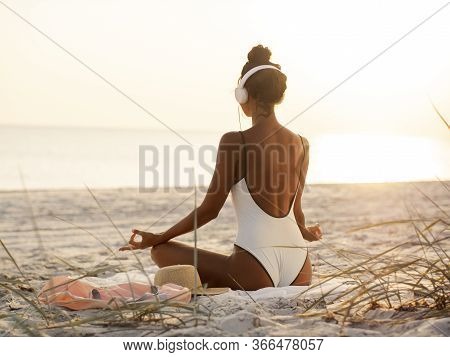 Young Beautiful Woman In Bikini Meditating And Listening To Calm Music In Yoga Lotus Pose On Deserte