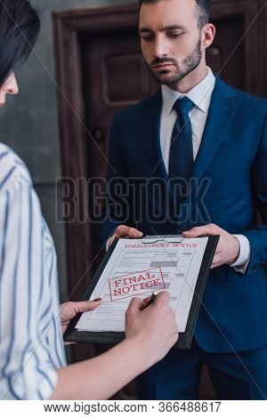 Woman Writing In Documents With Foreclosure And Final Notice Lettering Near Collector In Room