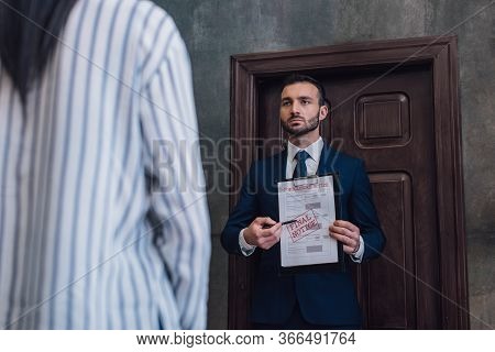 Collector Pointing With Pen At Documents With Foreclosure And Final Notice Lettering In Front Of Wom