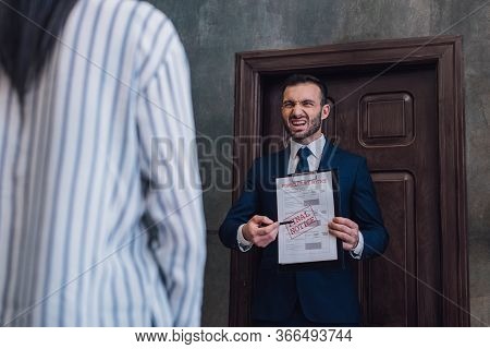 Angry Collector Pointing With Pen At Documents With Foreclosure And Final Notice Lettering In Front 