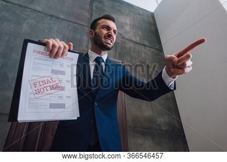 Low Angle View Of Angry Collector With Documents With Foreclosure And Final Notice Lettering Pointin
