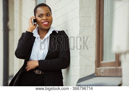 Talking On Phone. African-american Businesswoman In Office Attire Smiling, Looks Confident And Happy
