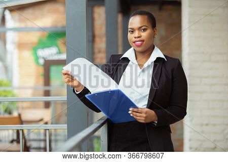 Paperwork. African-american Businesswoman In Office Attire Smiling, Looks Confident And Happy, Busy.