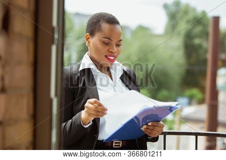 Paperwork. African-american Businesswoman In Office Attire Smiling, Looks Confident And Happy, Busy.