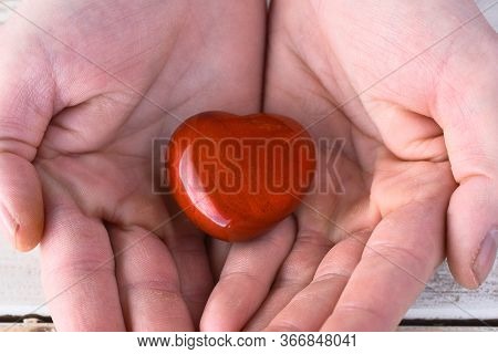 A Close Up Image Of A Hand Holding A Heart Shaped Red Jasper Healing Crystal.