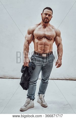 Athletic And Shirtless Male Model Posing In A Bright Studio, Showing His Embossed Body While Holding