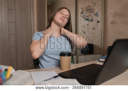 Tired Teen Girl Flexes Her Neck, Home Table Laptop, Distance Learning Education. Pain Muscle Fatigue
