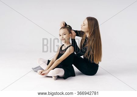 Mother Encourages Her Daughter Ballerina Sitting On The Floor On White Background.