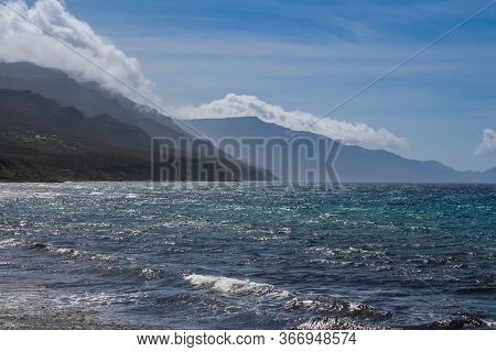 Waves Of The Mediterranean Sea With A White Foam. Sunny Spring Day With White Clouds On The Blue Sky