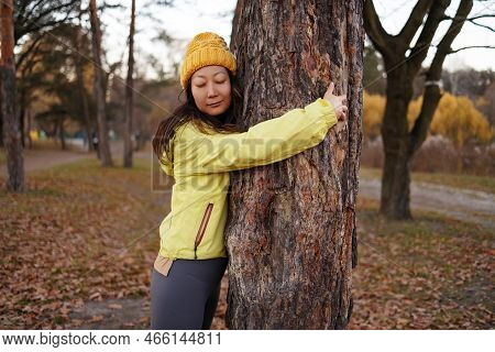 Happy Asian Girl Hug Tree Trunk In Outdoor Leisure Park Activity. Concept Of Environment And Ambient