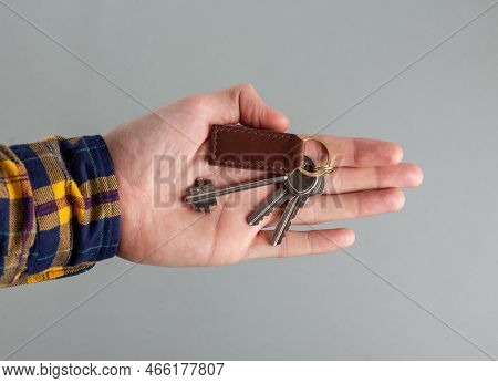 Keys With A Brown Leather Keychain In Hand On A Gray Background.