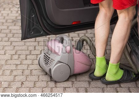 Man In Shorts And Green Socks Using Vacuum Cleaner Inside A Car. Domestic Male Chores. Cleaning Of A
