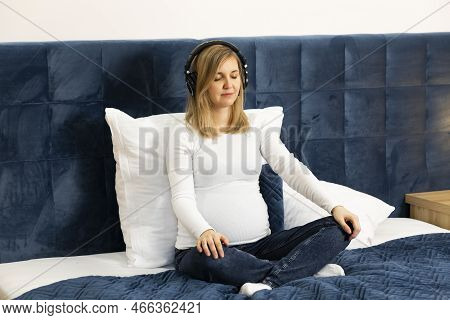 Pregnant Female With Headphones On Head, Listens To Hypnosis, Music, Meditates, Sitting On Bed. Baby