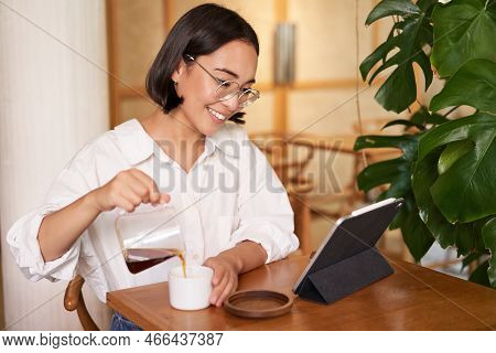 Freelance And Remote Workers. Smiling Young Woman Pouring Coffee In A Cup, Sitting In Cafe And Looki