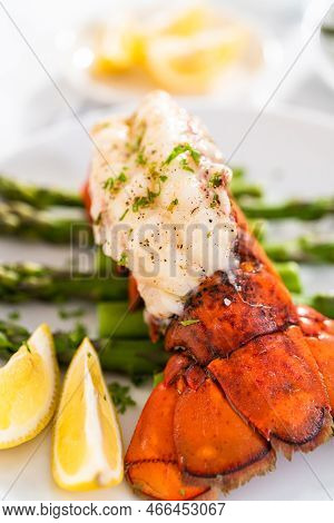 Sering Garlic Lobster Tails With Steamed Asparagus And Lemon Wedges On A White Plate.
