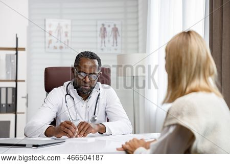 African American Doctor, Receives A Patient, Listens To Complaints, Makes Diagnostics. Writes Data. 