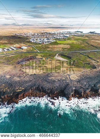 Vertical Photo Of Small Town In Iceland With Waves Crushing On The Shore In The Front