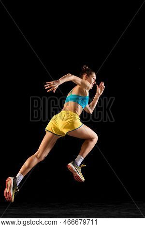 Back View. Sportive Muscled Woman, Professional Runner Running Away Isolated On Black Background. Sp