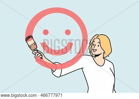 Girl Paints Smiling Face With Brush And Red Paint On Glass In Front Of Her. Blonde Young Woman Sprea