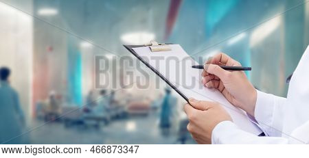 The Doctor Writes Information Into The Document Against The Backdrop Of The Hospital.