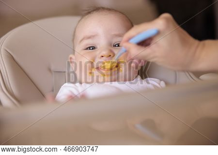 Mother Feeding Porridge To Her Happy Cheerful Baby Boy Using Spoon, Cheerful And Happy Baby Sitting 