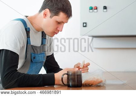 Lunch Break. Eating In Workplace During Work. Caucasian Man In Work Suit Sits At Table In Production