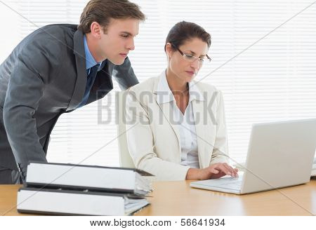Casal de negócios elegantemente vestida concentrado usando o laptop na mesa de escritório