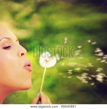  a pretty woman blowing on dandelion weed flowers 
