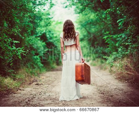 Young Woman With Suitcase In Hand Going Away By Rural Road