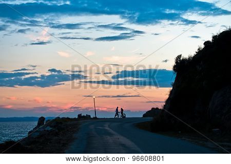 Young couple with tandem bicycle at sea coast after sunset