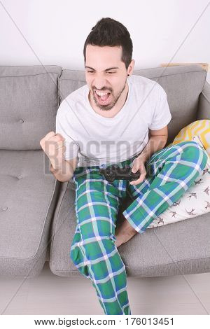Portrait of young man playing videogames and sitting on couch. Indoors.