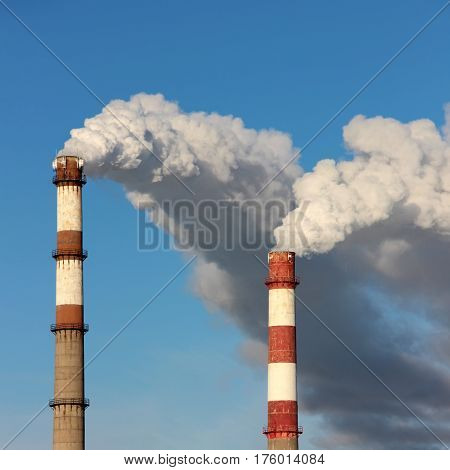 Dense clouds of smoke or steam out of two pipes on the background of blue sky. The concept of ecology pollution of the environment.