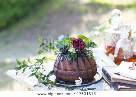 Cocolate cake decorated with flowers and three whiskey decanters against a light gray background with copy space