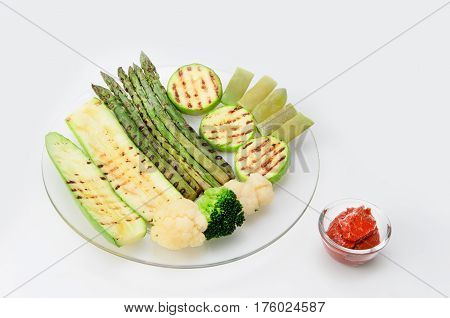 Grilled zucchini and asparagus, broccoli, lobi and cauliflower on a glass plate with red sauce