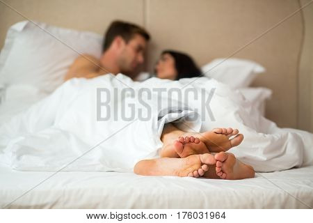 Feet of couple in bed. Man and woman under blanket. Warmth and comfort for two.