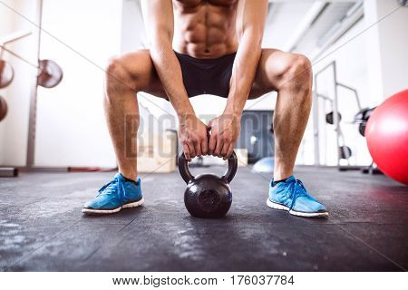 Unrecognizable young fit man doing strength training, doing squats with kettlebell in crossfit gym