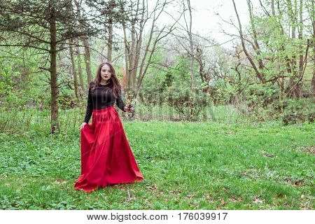 mystical witch woman in a red skirt with a candle in spring forest
