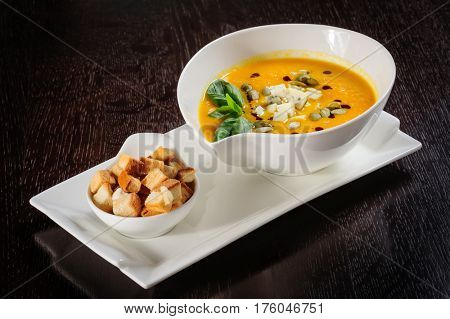 Roasted pumpkin soup with cream and pumpkin seeds on dark wooden background. Copy space.