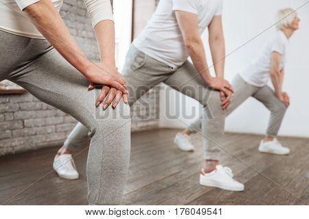 Try to repeat. Close up of hands touching knee that wearing grey trousers