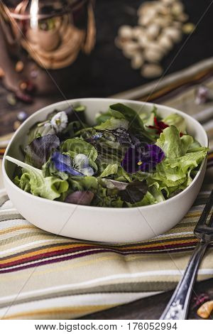 Spring green salad with edible flowers over a dark table
