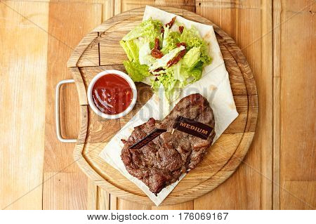 cooked steak on a pita a wooden board standing next to a gravy boat with ketchup and greens