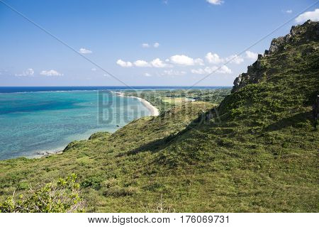Green slope leading to a turquoise green sea under sky in Ishigaki island