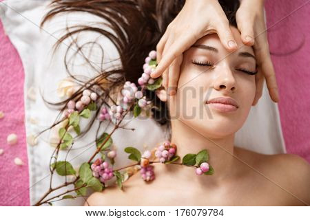 Top view of young beutiful woman at spa lying with tender flowers white facial massage